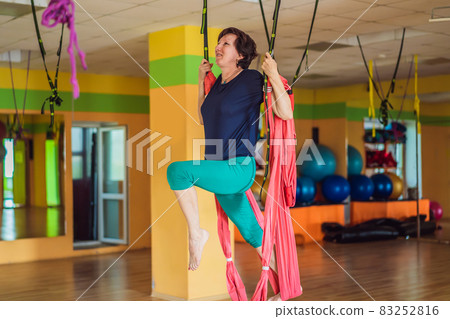 Senior mature woman practices anti-gravity yoga with a hammock in a studio. Lifestyle Senior mature woman practices anti-gravity yoga with a hammock in a studio. Lifestyle 83252816