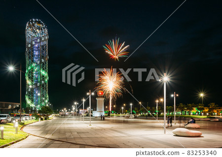 Batumi, Adjara, Georgia. Illuminated Alphabet Tower And Pitsunda Lighthouse At Promenade Near Miracle Park, Amusement City Park On Blue Evening Sky Background. Modern Urban Architecture 83253340