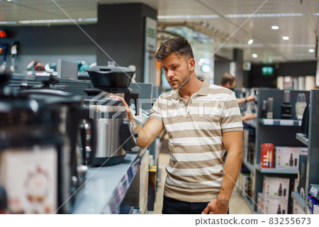 Male customer in striped t shirt touching and selecting new multicooker from shelf while shopping in mall Male customer in striped t shirt touching and selecting new multicooker from shelf while shopping in mall 83255673