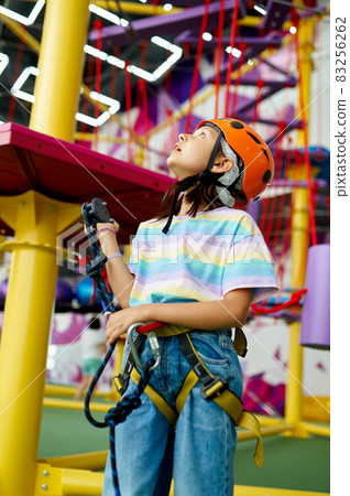 Cheerful little girl in helmet poses on zip line Cheerful little girl in helmet poses on zip line 83256262