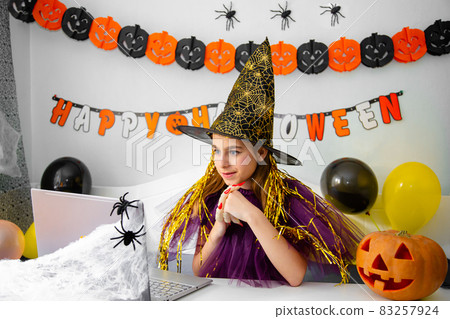 Halloween holiday concept. Cute little girl in witch costume sitting behind a table in Halloween theme decorated room. Halloween holiday concept. Cute little girl in witch costume sitting behind a table in Halloween theme decorated room. 83257924