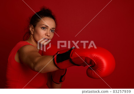 Boxer female athlete fights in red boxing gloves on a red background. Martial art concept with copy space for advertisement for boxing day event 83257939