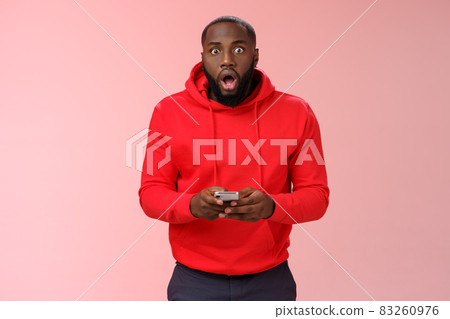 Amused overhwelmed black bearded guy in red hoodie drop jaw gasping widen eyes staring camera impressed holding smartphone using amazing cool game astonished new phone features, standing pink wall Amused overhwelmed black bearded guy in red hoodie drop jaw gasping widen eyes staring camera impressed holding smartphone using amazing cool game astonished new phone features, standing pink wall 83260976