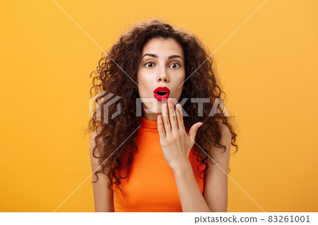 Waist-up shot of amazed and excited caucasian woman with curly hair in red lipstic opening mouth from surprise covering it with palm listening shocking rumors reacting astonished to amusing news Waist-up shot of amazed and excited caucasian woman with curly hair in red lipstic opening mouth from surprise covering it with palm listening shocking rumors reacting astonished to amusing news 83261001