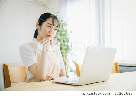 A woman in an apron using a computer (thinking / troubled) 83262683