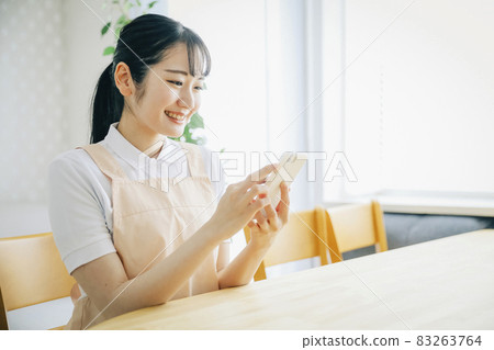 A woman in an apron using a smartphone 83263764