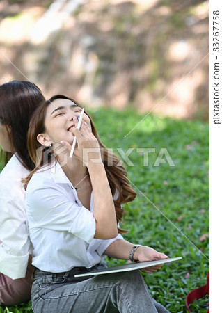 Cheerful asian woman sitting with her friend in the park. 83267758