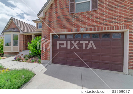 Facade of garage with brick wall and wide brown wooden door with glass panes Facade of garage with brick wall and wide brown wooden door with glass panes 83269027