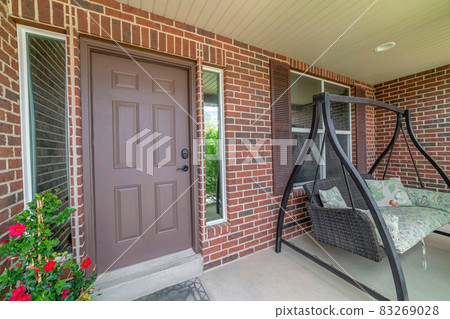 Home facade with brown front door between sidelights and swing bench on porch Home facade with brown front door between sidelights and swing bench on porch 83269028