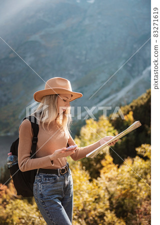Wanderlust and travel concept. Stylish traveler girl in hat looking at map, exploring woods. Wanderlust and travel concept. Stylish traveler girl in hat looking at map, exploring woods. 83271619