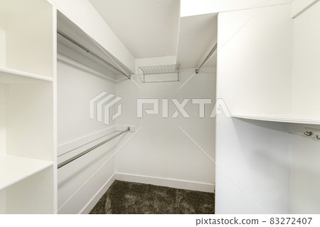 Interior of a plain white walk in closet with shelvings and carpeted floor Interior of a plain white walk in closet with shelvings and carpeted floor 83272407