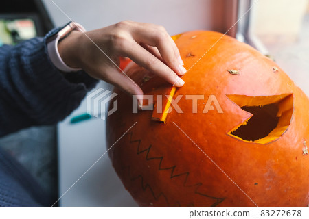 Hand of a young woman cutting out a Halloween pumpkin Hand of a young woman cutting out a Halloween pumpkin 83272678