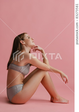 Full-length vertical portrait of young attractive girl posing in gray underwear isolated over pink background. 83273581