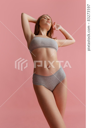 Cropped portrait of beautiful young woman in gray underwear posing isolated over pink background Cropped portrait of beautiful young woman in gray underwear posing isolated over pink background 83273597