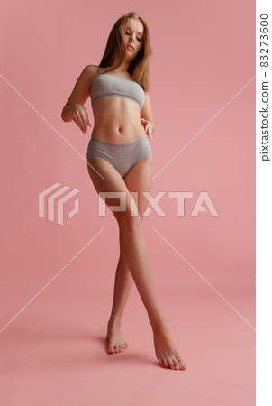 Full-length bottom view portrait of beautiful young woman in gray underwear posing isolated over pink background Full-length bottom view portrait of beautiful young woman in gray underwear posing isolated over pink background 83273600
