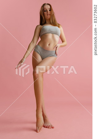 Full-length bottom view portrait of beautiful young woman in gray underwear posing isolated over pink background Full-length bottom view portrait of beautiful young woman in gray underwear posing isolated over pink background 83273602
