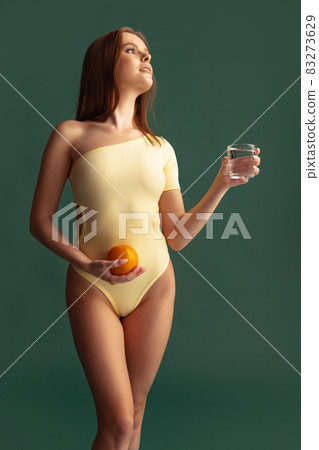 Cropped portrait of beautiful woman in yellow bodysuit posing isolated over green background Cropped portrait of beautiful woman in yellow bodysuit posing isolated over green background 83273629