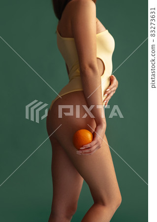 Cropped image of female body, side view in beige inner wear isolated over green background. Anti cellulite care Cropped image of female body, side view in beige inner wear isolated over green background. Anti cellulite care 83273631