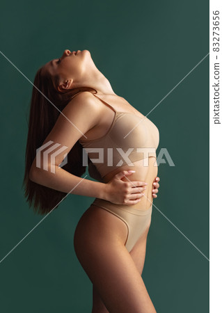 Cropped portrait of beautiful slim woman posing in beige underwear isolated over green background. Tenderness Cropped portrait of beautiful slim woman posing in beige underwear isolated over green background. Tenderness 83273656
