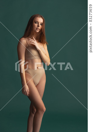 Full-length portrait of beautiful tender woman posing in beige underwear isolated over green background. Femininity Full-length portrait of beautiful tender woman posing in beige underwear isolated over green background. Femininity 83273659