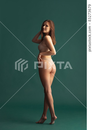 Full-length portrait of beautiful tender woman posing in beige underwear isolated over green background, back view Full-length portrait of beautiful tender woman posing in beige underwear isolated over green background, back view 83273679
