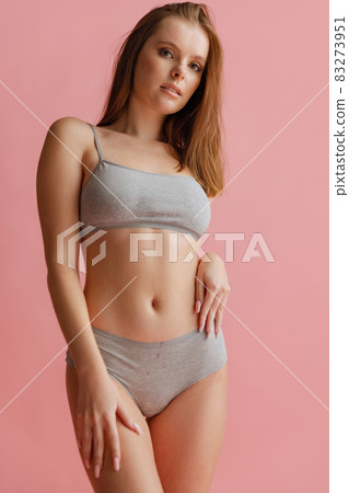 Cropped portrait of beautiful young woman in gray underwear posing isolated over pink background. Cropped portrait of beautiful young woman in gray underwear posing isolated over pink background. 83273951