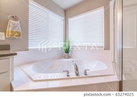 Built in bathtub at the corner of a well lighted home bathroom with two windows Built in bathtub at the corner of a well lighted home bathroom with two windows 83274025