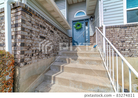 Blue front door with wreath and concrete stairs at the entrance of sunlit home 83274811