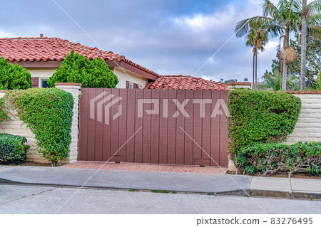 Brown gate and white brick fence against red tile roof of house in San Diego CA 83276495