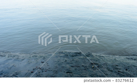 Muddy river banks in low tide next to wave water. Alluvial soils deposited by the river. Nature background. Close up. Muddy river banks in low tide next to wave water. Alluvial soils deposited by the river. Nature background. Close up. 83276612