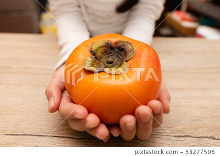 Hand of a child holding a persimmon 83277508