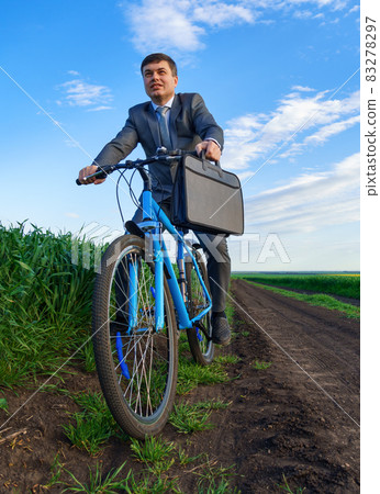 Businessman rides a bicycle in a green grass field - business concept for freedom, vacation or freelance. Beautiful spring nature. Businessman rides a bicycle in a green grass field - business concept for freedom, vacation or freelance. Beautiful spring nature. 83278297