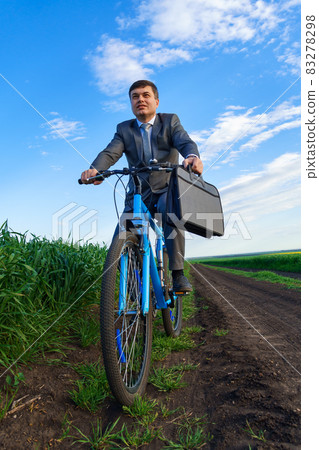 Businessman rides a bicycle in a green grass field - business concept for freedom, vacation or freelance. Beautiful spring nature. Businessman rides a bicycle in a green grass field - business concept for freedom, vacation or freelance. Beautiful spring nature. 83278298