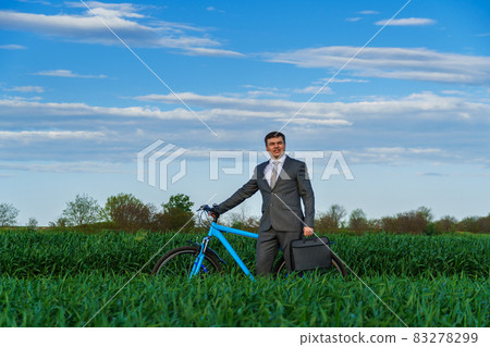 Businessman rides a bicycle in a green grass field - business concept for freedom, vacation or freelance. Beautiful spring nature. Businessman rides a bicycle in a green grass field - business concept for freedom, vacation or freelance. Beautiful spring nature. 83278299
