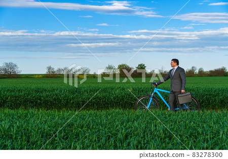 Businessman rides a bicycle in a green grass field - business concept for freedom, vacation or freelance. Beautiful spring nature. Businessman rides a bicycle in a green grass field - business concept for freedom, vacation or freelance. Beautiful spring nature. 83278300
