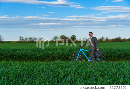 Businessman rides a bicycle in a green grass field - business concept for freedom, vacation or freelance. Beautiful spring nature. Businessman rides a bicycle in a green grass field - business concept for freedom, vacation or freelance. Beautiful spring nature. 83278301