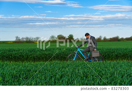Businessman rides a bicycle in a green grass field - business concept for freedom, vacation or freelance. Beautiful spring nature. Businessman rides a bicycle in a green grass field - business concept for freedom, vacation or freelance. Beautiful spring nature. 83278303