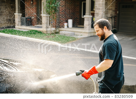Cacuasian man washing car by water jet in front of house at home. 83280509