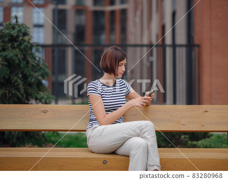 Smiling woman using mobile phone in the street Smiling woman using mobile phone in the street 83280968