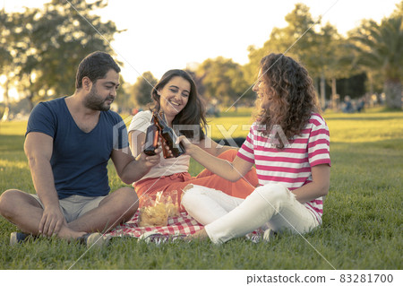 Three friends sitting on the grass in the park 83281700