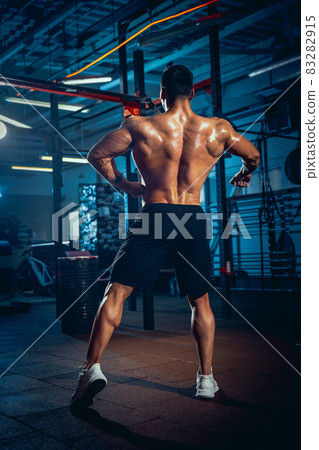 Portrait of young man, muscled athlete, bodybuilder posing at sport gym, indoors. Concept of sport, activity, healthy lifestyle Portrait of young man, muscled athlete, bodybuilder posing at sport gym, indoors. Concept of sport, activity, healthy lifestyle 83282915