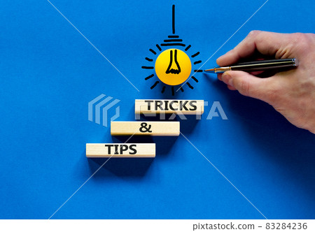 Tips and tricks symbol. Wooden blocks with words 'Tips and tricks'. Beautiful blue background. Businessman hand, yellow light bulb icon. Business, tips and tricks concept. Copy space. 83284236
