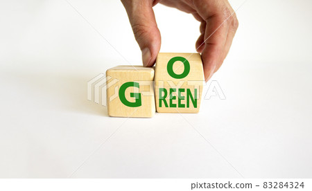 Ecology and go green symbol. Businessman turns a wooden cube with concept words 'Go green' on a beautiful white table, white background. Copy space. Business and go green concept. 83284324