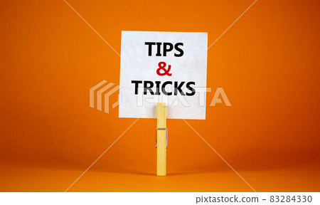 Tips and tricks symbol. White paper on wooden clothespin. Words 'Tips and tricks'. Beautiful orange background. Business and tips and tricks concept, copy space. 83284330