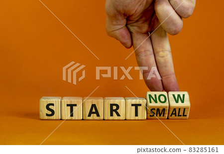 Start small and now symbol. Businessman turns wooden cubes and changes words 'start small' to 'start now'. Beautiful orange background, copy space. Business and start small and now concept. 83285161