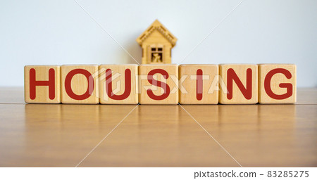 Blocks form the word housing in front of a miniature house. 83285275