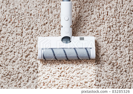 A cordless vacuum cleaner cleans the carpet in the living room with the bottom of the legs With a clean stripe 83285326