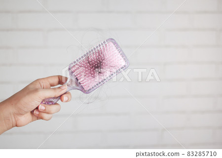 women hand hold a brush with lost hair against white wall  83285710