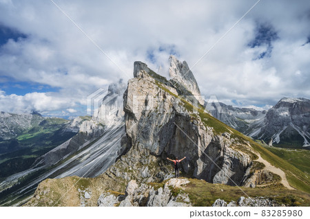 A man raising his hands in front of epic Furchetta and Sass Rigais peaks in Seceda, Dolomites Alps, Odle mountain range, South Tyrol, Italy, Europe. Travel vacation concept 83285980