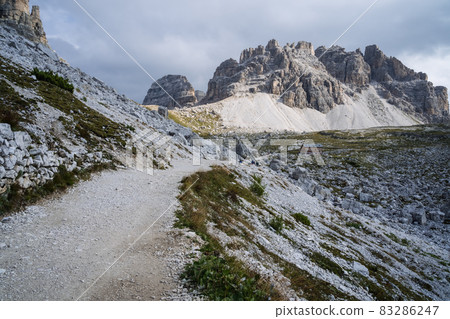 Hiking trail to Cime di Lavaredo with Cadini di Misurina mountain group in background. Dolomites, Italy Hiking trail to Cime di Lavaredo with Cadini di Misurina mountain group in background. Dolomites, Italy 83286247